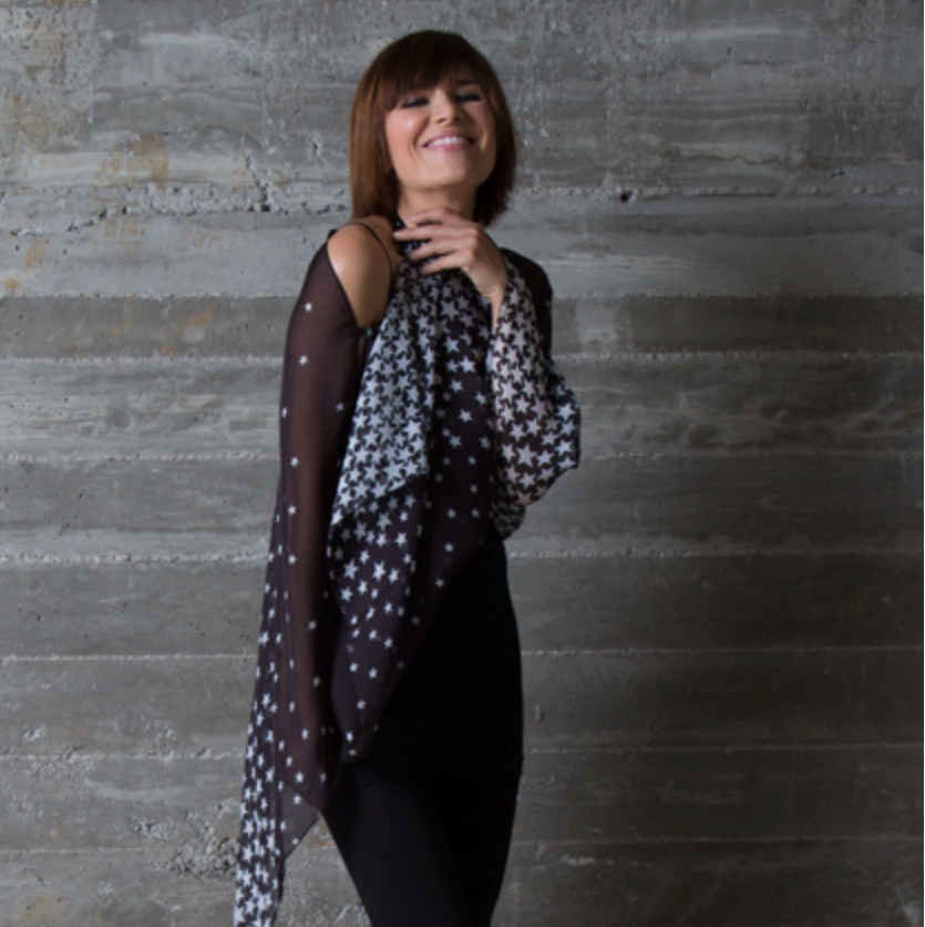 Woman wearing black and white star print silk LuLuWrap , smiling in front of gray concrete was