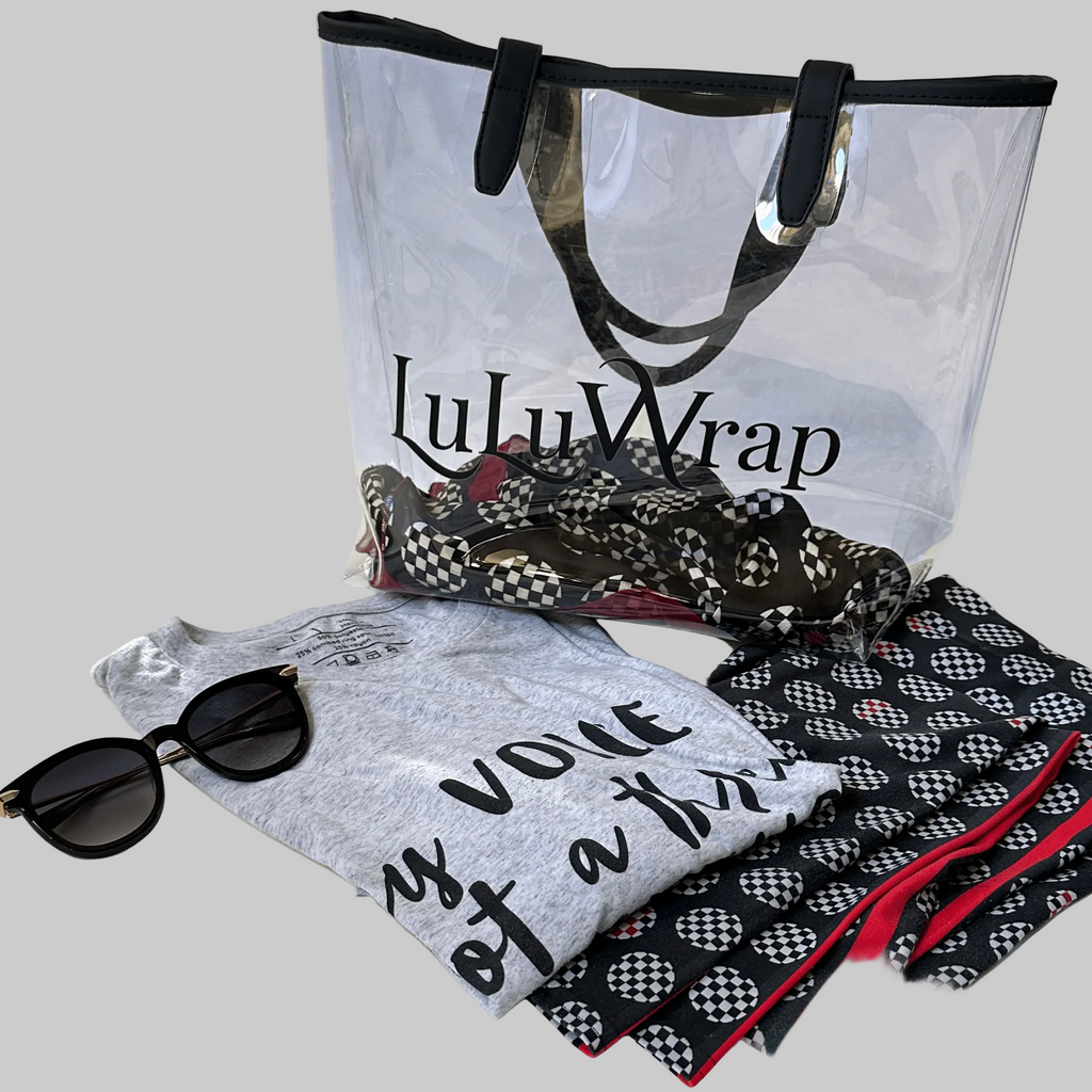 Clear plastic tote with black handles The LuLuwrap logo is written in black on bag . A LuLuwrap is inside the bag and a LuLuWrap tee shirt and leggings is laid out in front of the bag