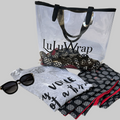 Clear plastic tote with black handles The LuLuwrap logo is written in black on bag . A LuLuwrap is inside the bag and a LuLuWrap tee shirt and leggings is laid out in front of the bag