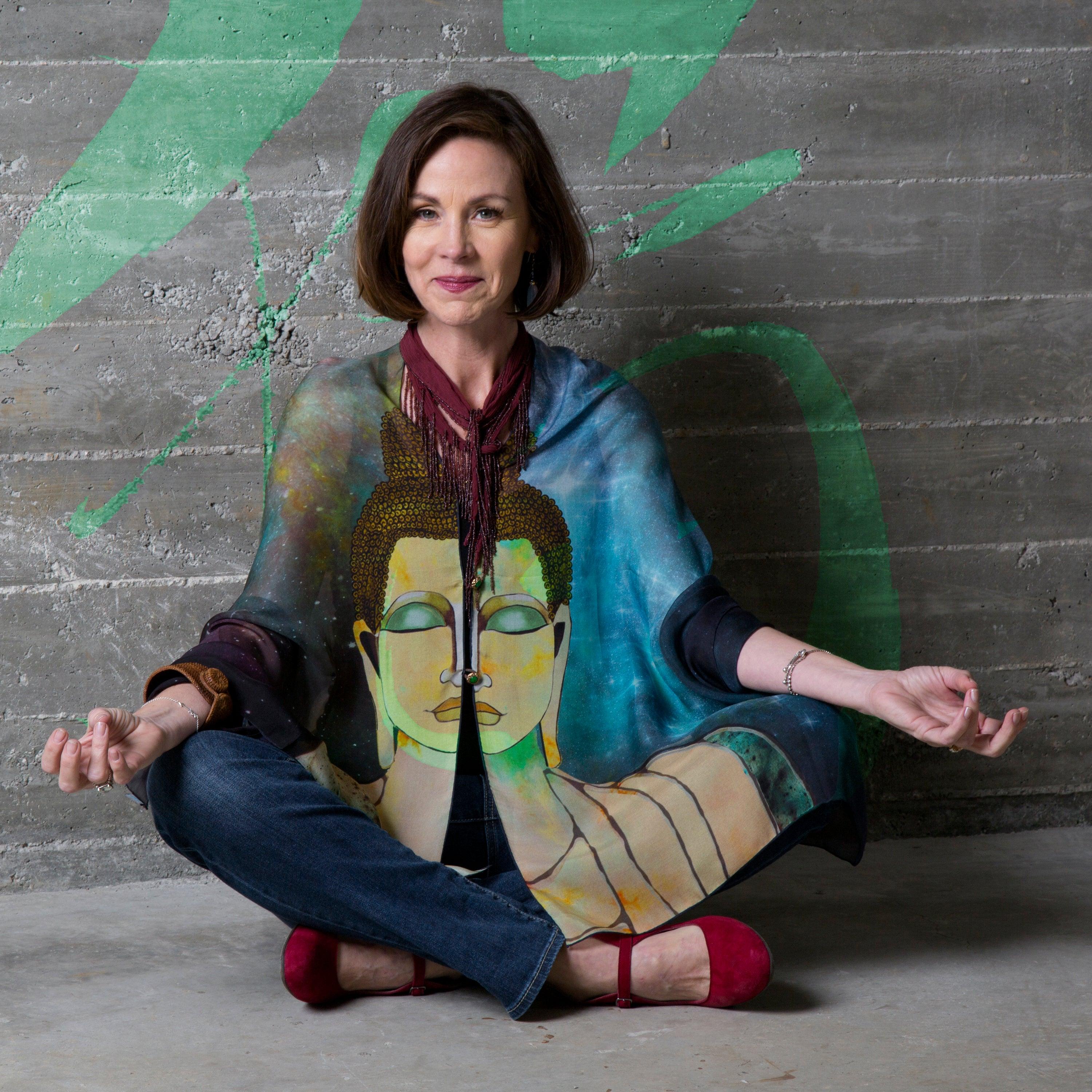 Woman in lotus pose in front of decorated gray wall wearing Buddha Luuwraps as a blouse